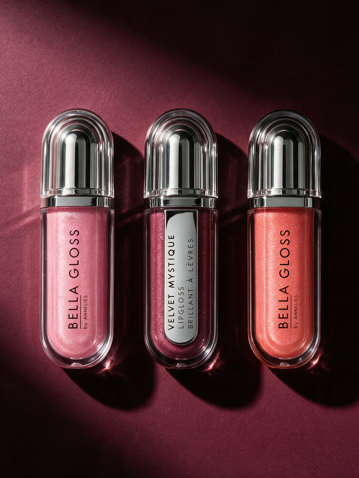 The three Bella Gloss Set shades seen from above, side by side on a deep red surface