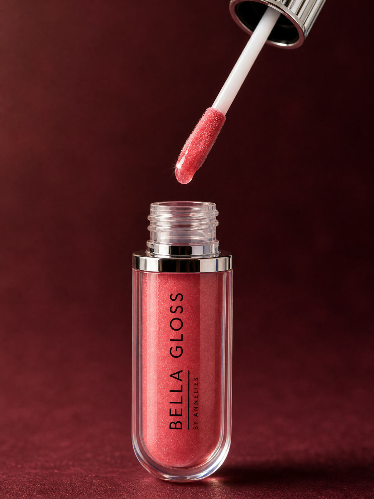 The Bella Gloss lip gloss applicator hovers above the open tube, loaded with gloss